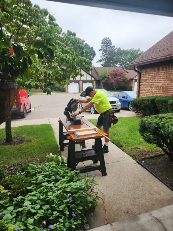A carpenter cutting trim on a miter saw set up on a front walk