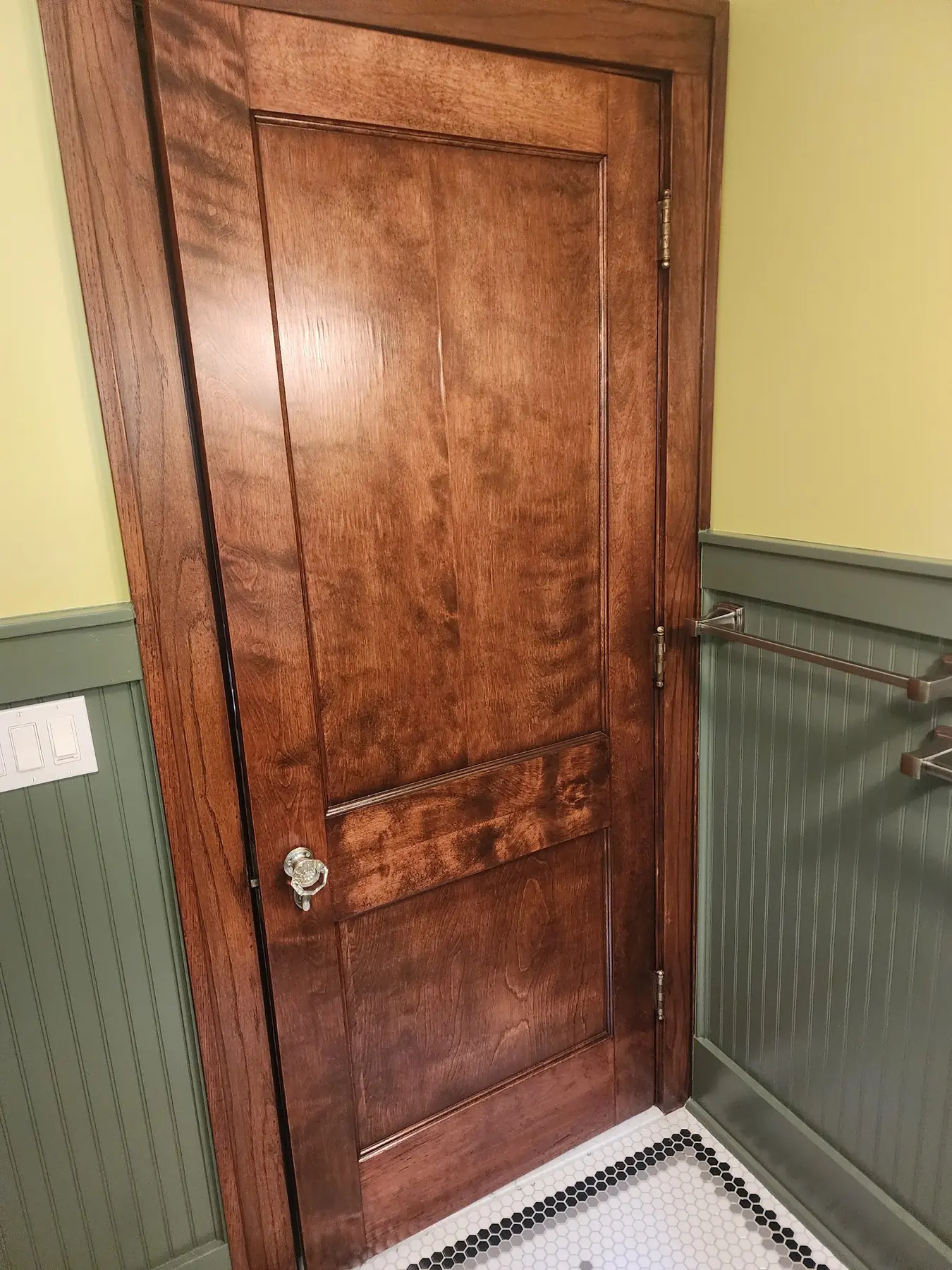 The same door finished: richly figured wood and a glass knob, green beadboard wainscot and yellow walls