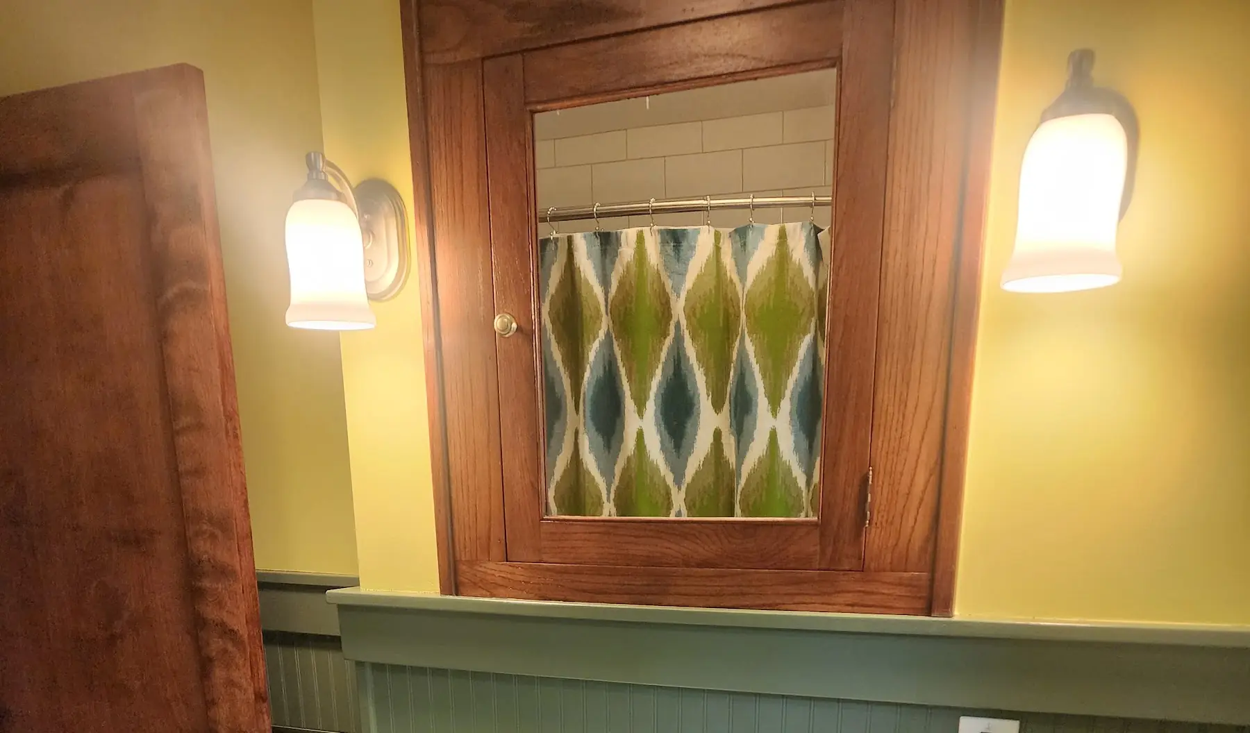 The same wall finished: yellow paint, green beadboard and the medicine cabinet between two sconces