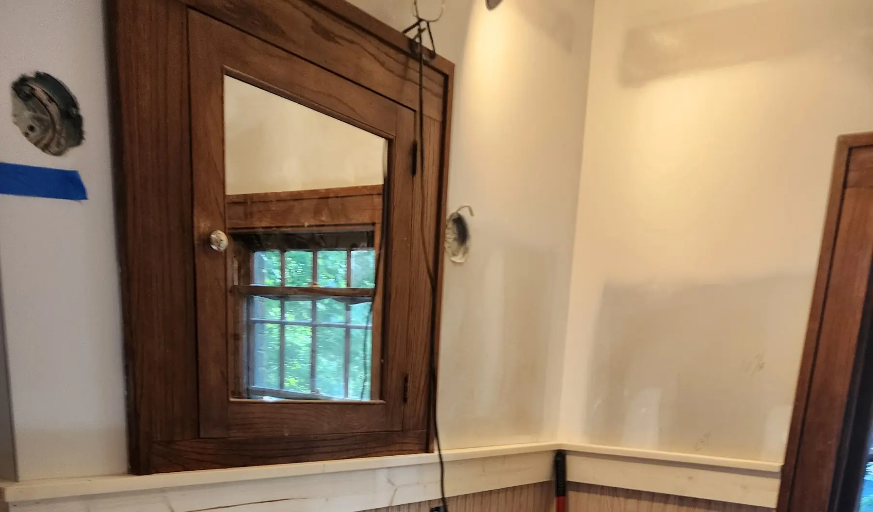 Wood medicine cabinet on bare drywall above unpainted beadboard, mid-renovation