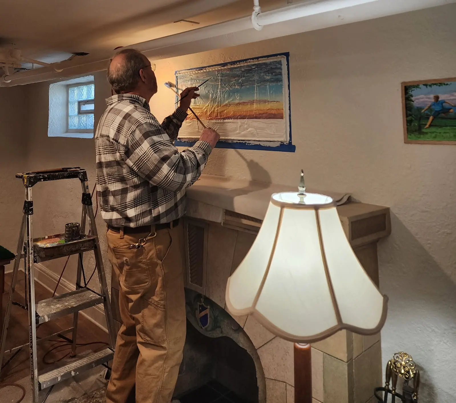 John Sames painting a panel above a fireplace