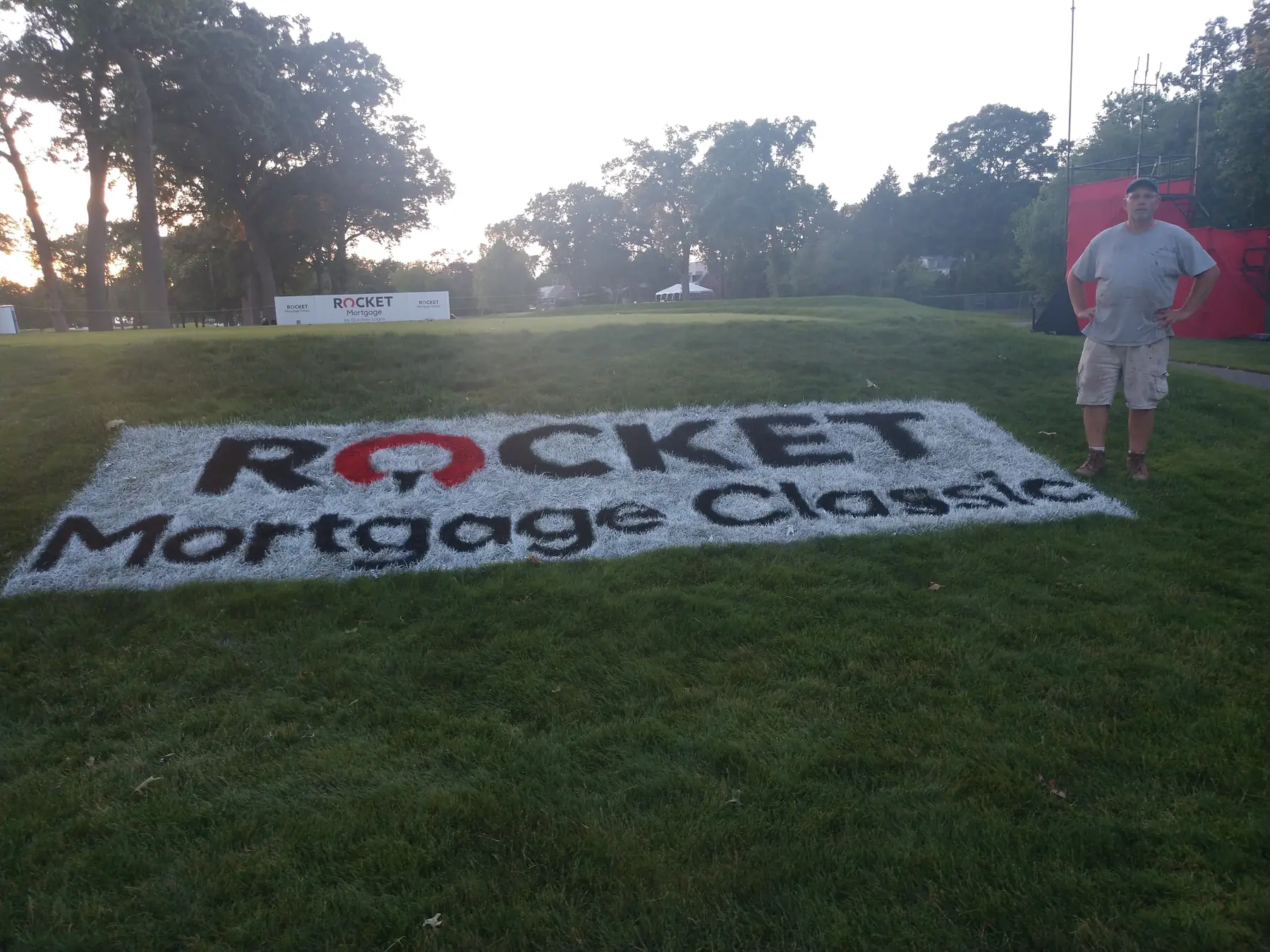 The Rocket Mortgage Classic turf logo at dusk with a man standing beside it